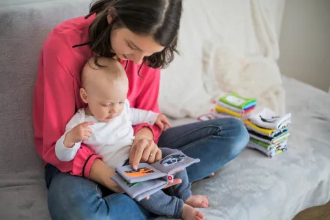 White background with a woman reading a book to a baby.