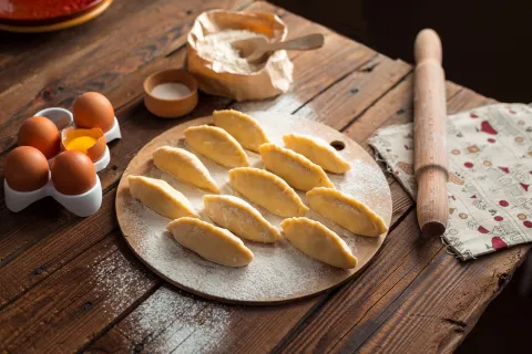 Black background with a brown wood table.  Table has a white plate with baked goods.  There are eggs and a rolling pin on the table.