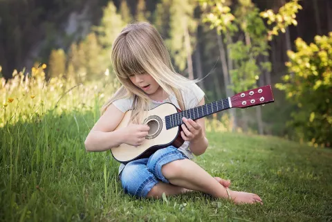 Green background with a child sitting in the grass playing a guitar.