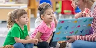 Two children sitting with a teacher reading a book.