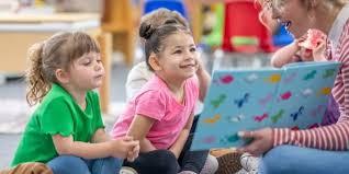 Two children sitting with a teacher reading a book.